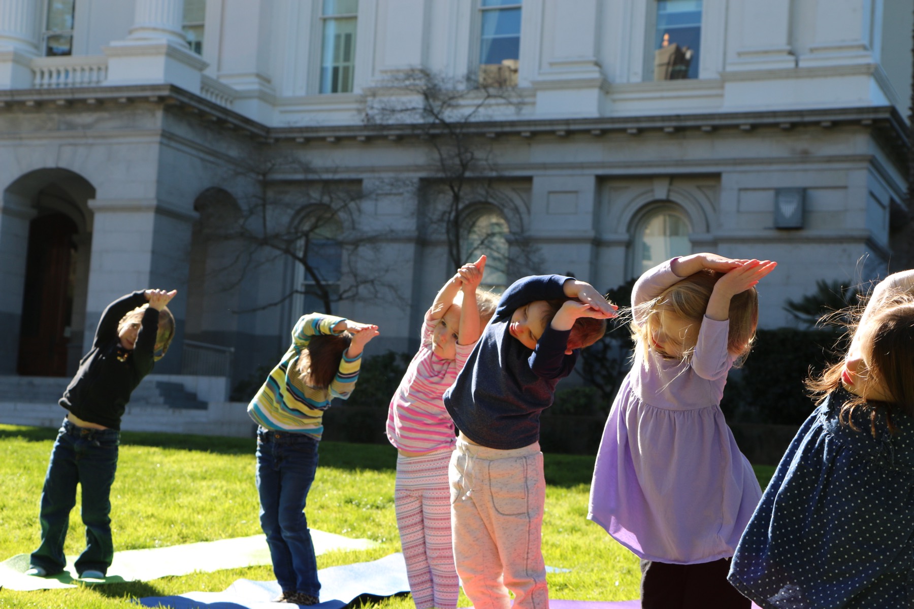 Preschoolers in a side-bend yoga pose during a mindfulness practice on the California State Capitol lawn at Growing Mindfully Sacramento.