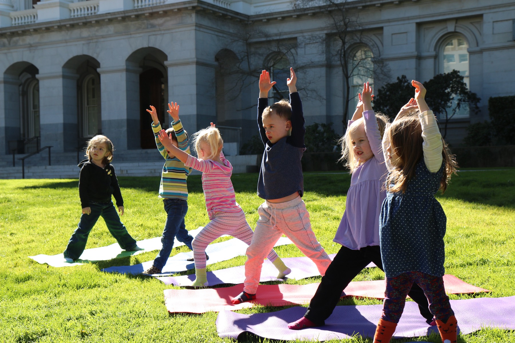 Preschoolers in a joyful warrior pose with arms raised at Growing Mindfully Sacramento.