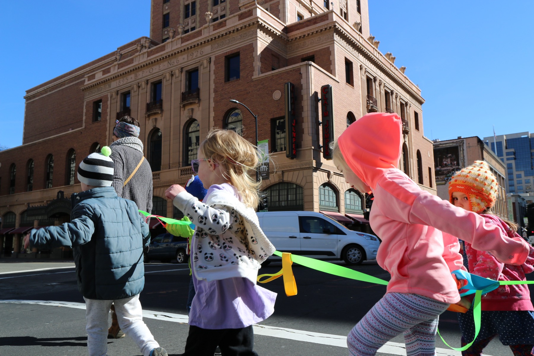 Children walking together with a colored ribbon in downtown Sacramento, near Growing Mindfully.